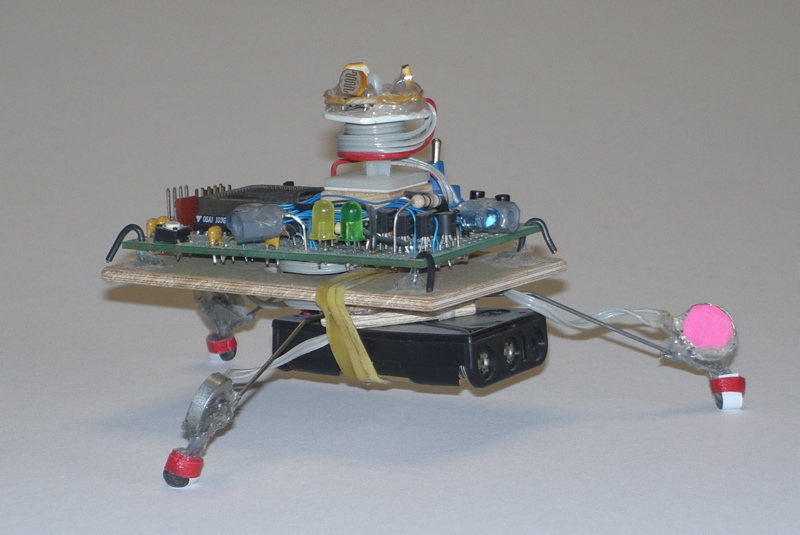 Crazy Legs robot viewed from the side, showing the circuit board with the photo sensors on top,
        the batties underneath, and the legs sticking out to the side